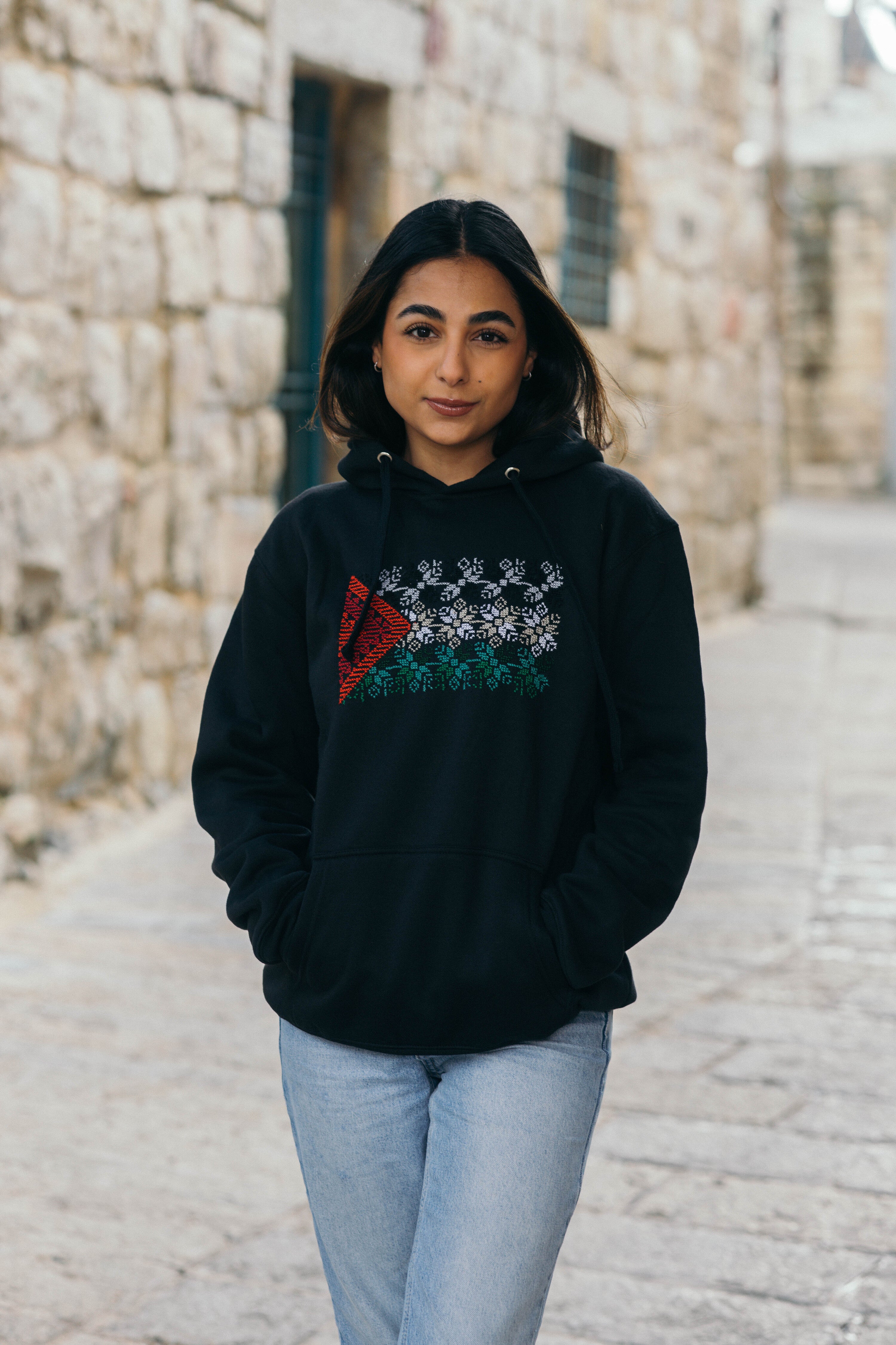 Person wearing a black hoodie with a design on a stone-paved street.