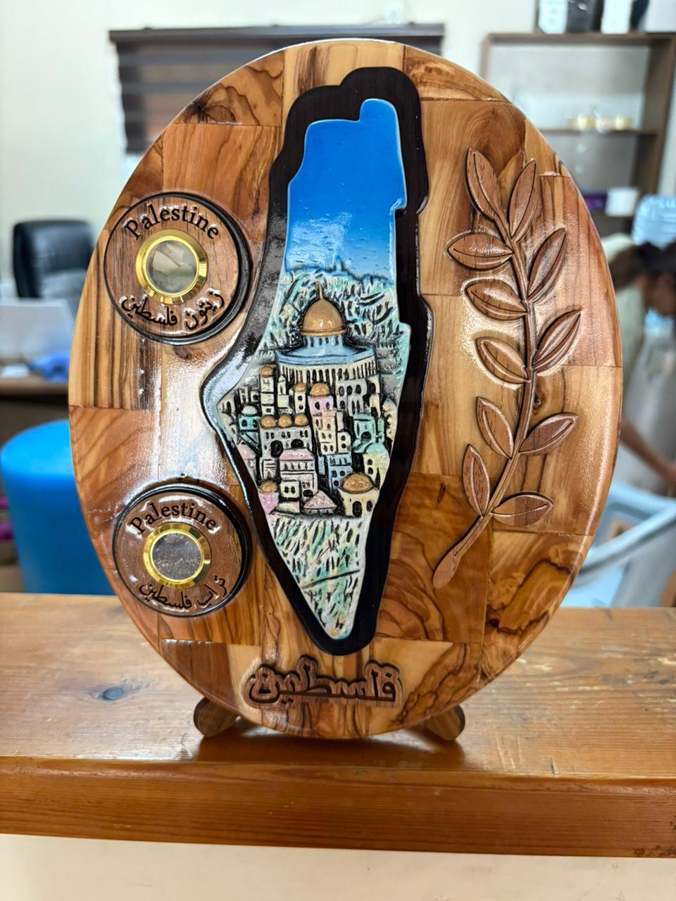 Wooden plaque with artistic depiction of a city, surrounded by nature elements, on a wooden surface.